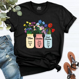 May include: Black t-shirt with a design of three mason jars filled with colorful flowers. Each jar has a label that says "Mom", "Grandma", and "Great-Grandma" with names listed underneath.