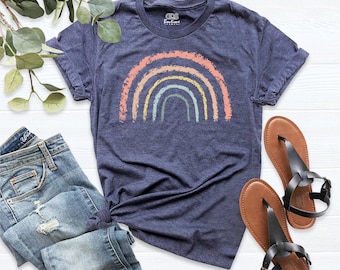 May include: A heather navy blue short-sleeve t-shirt featuring a distressed rainbow graphic in muted tones of peach, yellow, and sage green. The shirt has a crew neckline and a small interior label that reads ODS Boutique.