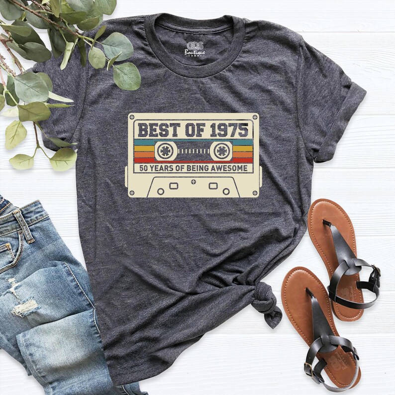 K&ouml;nnte beinhalten: Ein dunkelgraues T-Shirt mit einer Vintage-Kassettengrafik, auf der "Best of 1975" und "50 Years of Being Awesome" steht.