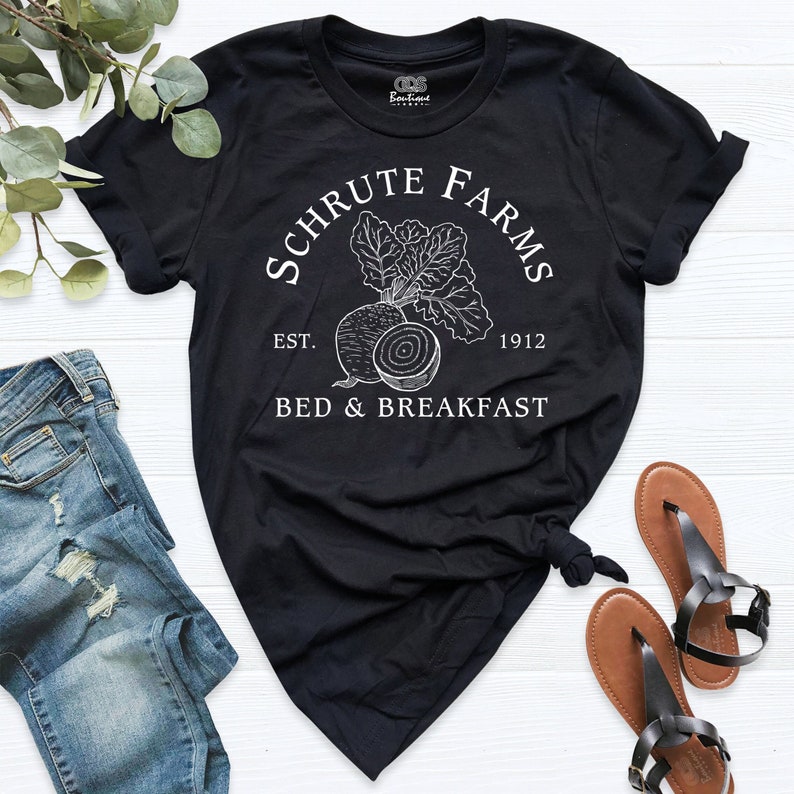 May include: Black t-shirt with white text that reads "Schrute Farms Est. 1912 Bed & Breakfast" with a drawing of a beet.