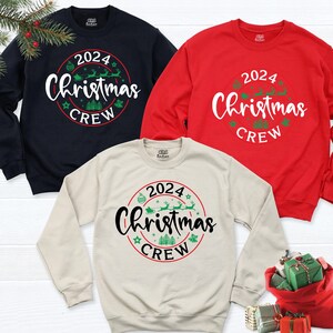 May include: Three Christmas crew sweatshirts in navy blue, red, and beige. Each sweatshirt features a circular design with the text "2024 Christmas Crew" in green and white lettering.
