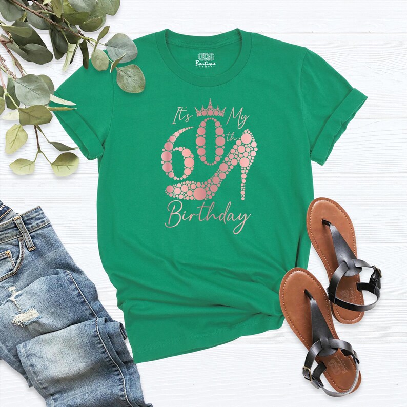 May include: Green t-shirt with the text "It's My 60th Birthday" in a rose gold font. The number 60 is made up of a high heel shoe with a crown on top.