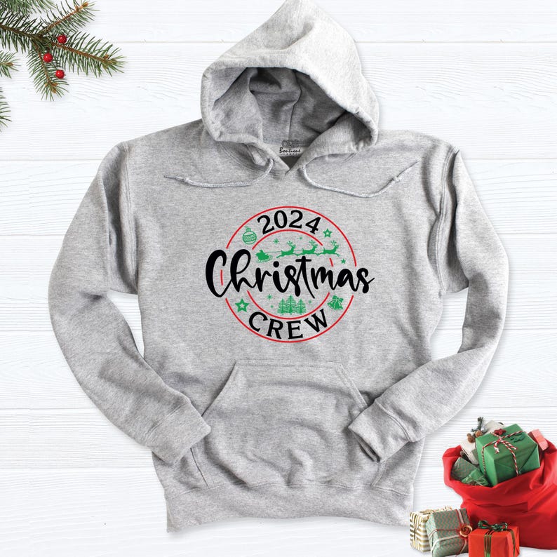 May include: Grey hooded sweatshirt with a red circle graphic that says "2024 Christmas Crew" with green Christmas-themed illustrations inside the circle.