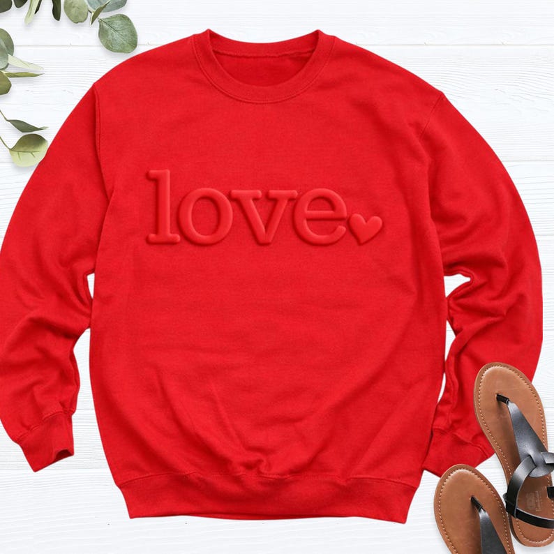 May include: A bright red sweatshirt with the word "love" embossed across the front. The word "love" is in a bold, sans-serif font, with a small heart replacing the "o". The sweatshirt has a crew neck and long sleeves.