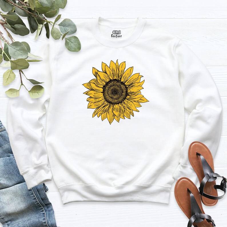 May include: White sweatshirt with a yellow sunflower graphic. The sunflower is drawn in black outline.