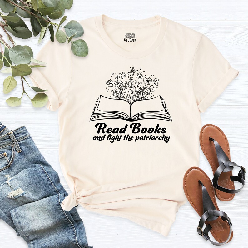 May include: A cream colored t-shirt with a black graphic of an open book with flowers growing out of it. The text "Read Books and fight the patriarchy" is below the book.
