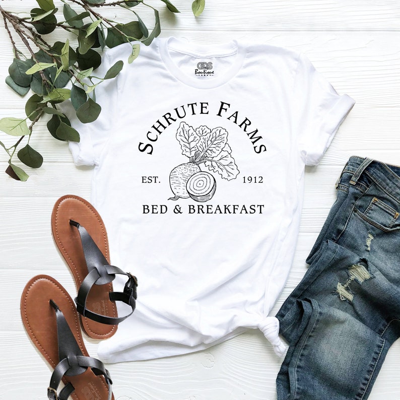 May include: White t-shirt with a black and white graphic design of a beet with the text "Schrute Farms Est. 1912 Bed & Breakfast".