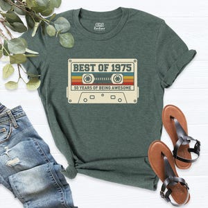 K&ouml;nnte beinhalten: Ein gr&uuml;nes T-Shirt mit einer Vintage-Kassettengrafik, auf der "Best of 1975" und "50 Years of Being Awesome" steht.
