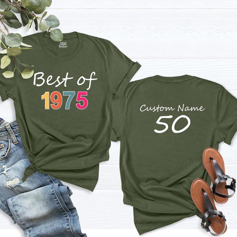 May include: Two olive green t-shirts. The front of one shirt says "Best of 1975" in rainbow colors. The back of the other shirt says "Custom Name 50" in white.