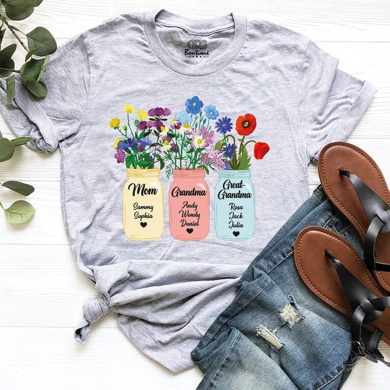 May include: Gray t-shirt with a floral design featuring three mason jars labeled "Mom", "Grandma", and "Great-Grandma". Each jar has a heart and names of family members written inside.