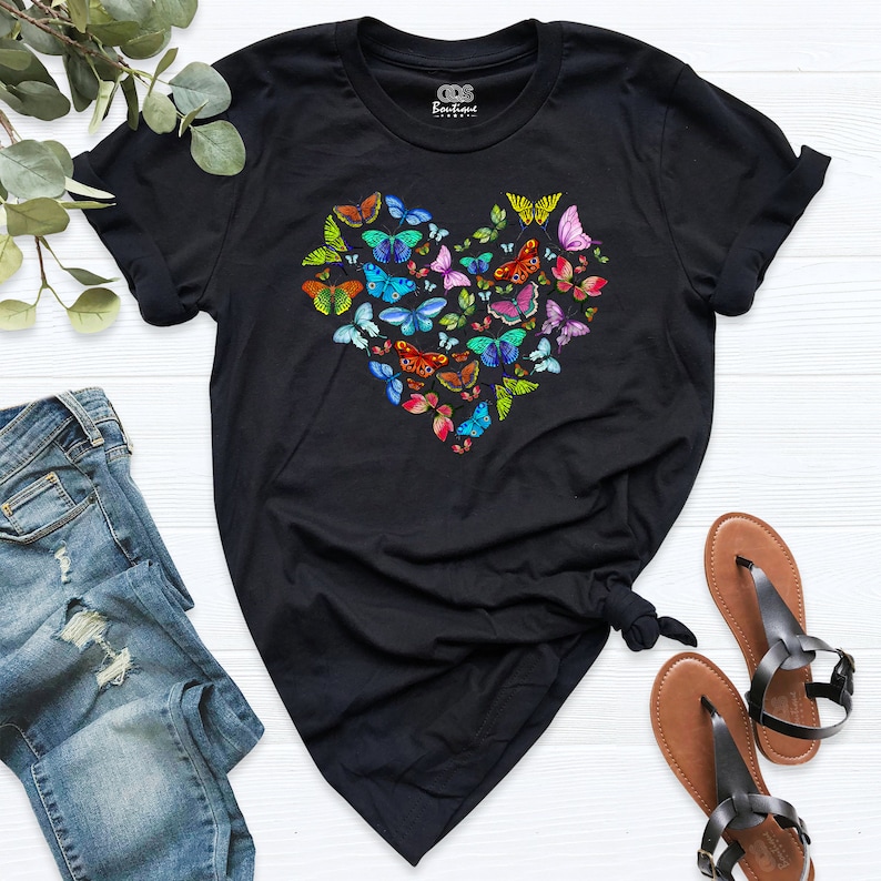 May include: Black t-shirt featuring a heart-shaped design made up of colourful butterflies. The butterflies are arranged in a heart shape and are all different colours and sizes.