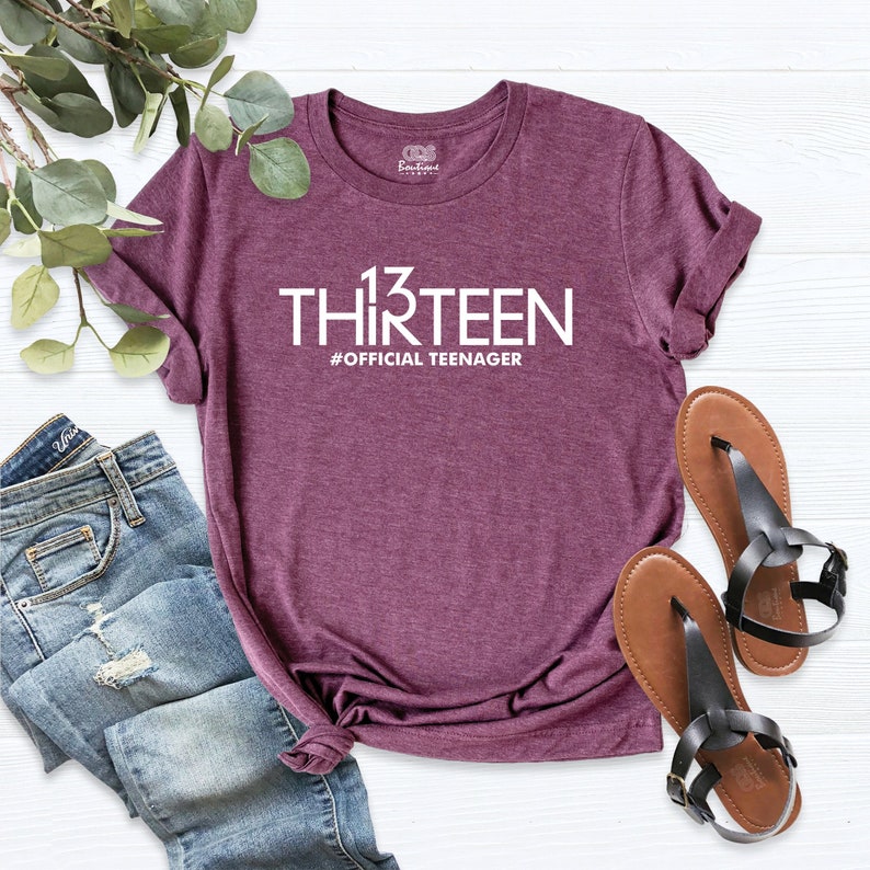 May include: A maroon t-shirt with the text "13 THIRTEEN #OFFICIAL TEENAGER" printed in white.