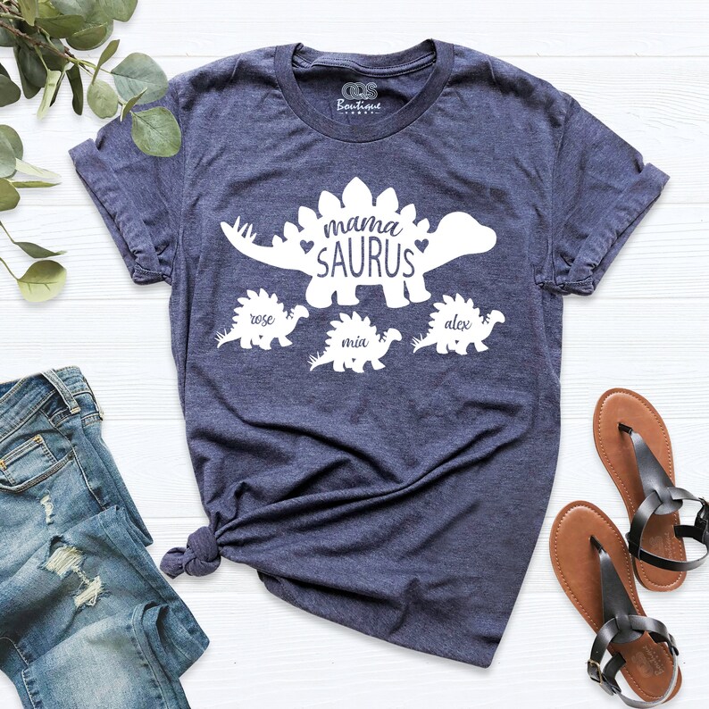 May include: A navy blue t-shirt with a white dinosaur graphic that says "mama saurus" with three smaller dinosaurs below it that say "rose", "mia", and "alex".