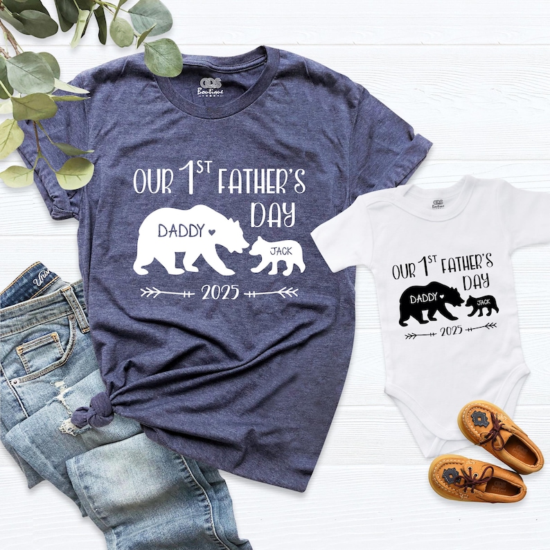 Pu&ograve; includere: T-shirt blu navy e body bianco con grafica abbinata dell'orso "Our 1st Father's Day". La t-shirt ha il testo "Daddy" e il body "Jack" sotto la grafica dell'orso. L'anno "2025" &egrave; stampato su entrambi.