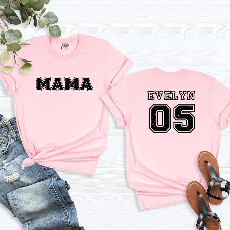 May include: Two pink t-shirts with black text. One shirt says "MAMA" and the other says "EVELYN 05".