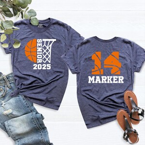 May include: Two navy blue t-shirts with basketball-themed designs. The front shirt has a basketball and hoop with the text "Senior 2025". The back shirt has a basketball with the number "14" and the text "Marker".