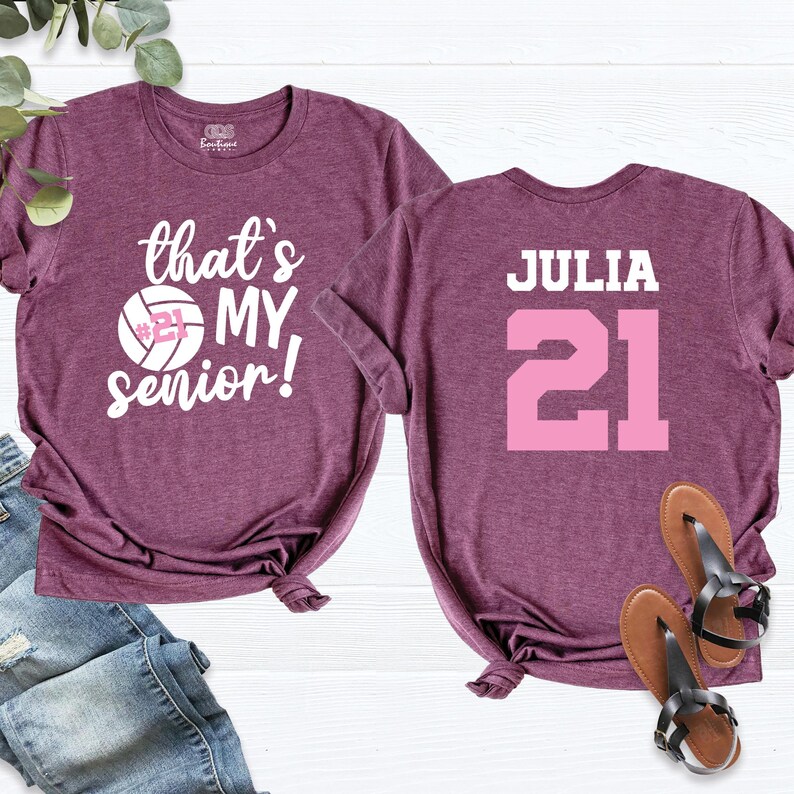 May include: Two maroon t-shirts. One shirt has the text "that's my senior!" with a volleyball and the number 21. The other shirt has the name "JULIA" and the number 21 in pink.