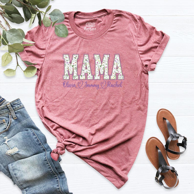 Puede incluir: Una camiseta color malva con un estampado floral de "MAMA" y los nombres Olivia, Sammy y Rachel impresos debajo.