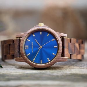 May include: A wooden wristwatch with a blue face and gold accents. The watch has a wooden band and a gold crown. The watch face features gold hands and markers. The watch is a stylish accessory.