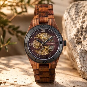 May include: A wooden wristwatch with a dark burgundy face and a visible mechanical movement. The watch has a dark gray bezel and a wooden band. The watch face displays Roman numerals and the brand name "WOODPECKER".