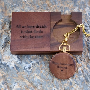 May include: A wooden box with a quote engraved on the front: "All we have decide is what do do with the time". The box is open and a wooden pocket watch with a gold chain is inside. The pocket watch has the words "Happy Anniversary I love you" engraved on the front.