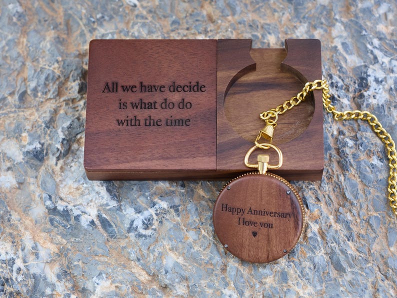 May include: A wooden box with a quote engraved on the front: "All we have decide is what do do with the time". The box is open and a wooden pocket watch with a gold chain is inside. The pocket watch has the words "Happy Anniversary I love you" engraved on the front.