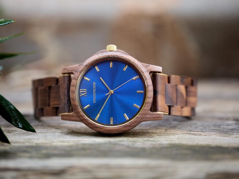 May include: A wooden wristwatch with a blue face and gold accents. The watch has a wooden band and a gold crown. The watch face features gold hands and markers. The watch is a stylish accessory.