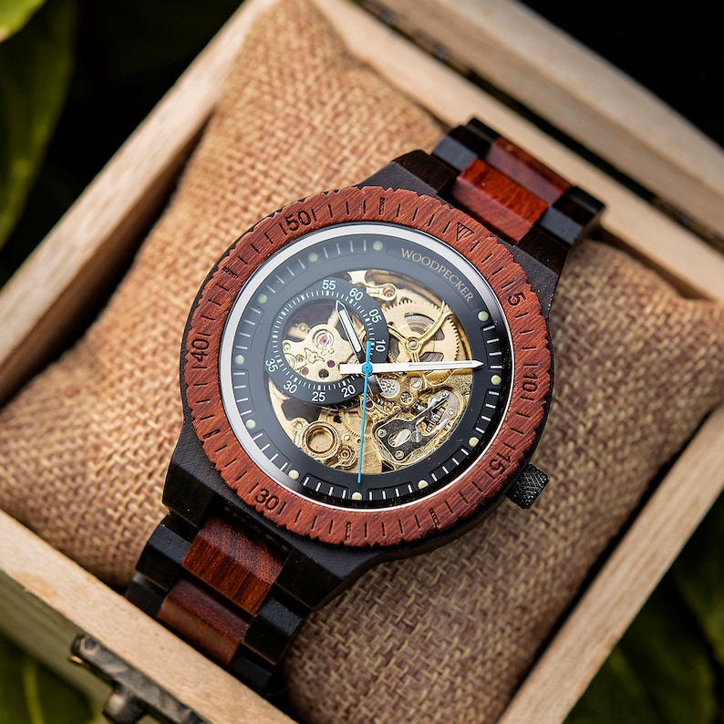 May include: A black and red wooden wristwatch with a skeleton dial and the word "WOODPECKER" printed on the face.