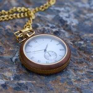 May include: A gold pocket watch with a brown wooden case and a white face with Roman numeral markings. The watch has a gold chain attached to it.