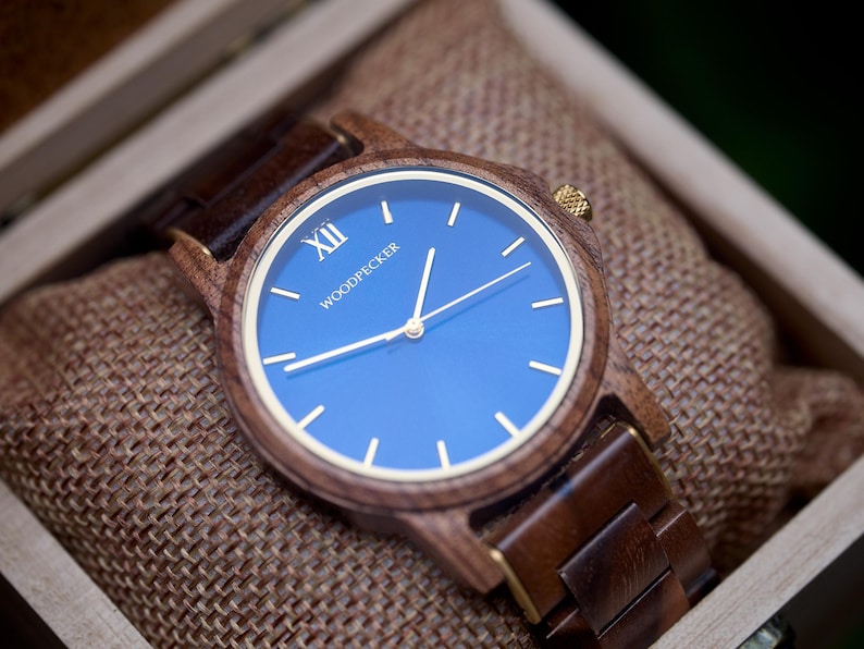May include: Wooden wristwatch with a blue face and gold-colored hands and accents. The watch is in a wooden box with a burlap lining. The watch face has the word "WOODPECKER" printed on it.