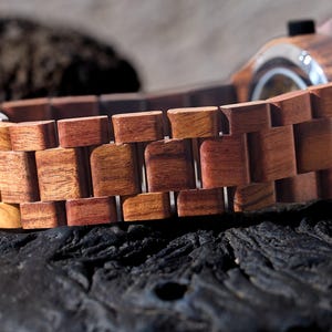 Puede incluir: Primer plano de una correa de reloj de madera de color marr&oacute;n rojizo. La correa est&aacute; hecha de eslabones de madera individuales que est&aacute;n conectados entre s&iacute;.
