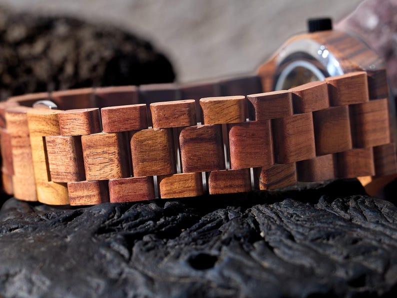 Puede incluir: Primer plano de una correa de reloj de madera de color marr&oacute;n rojizo. La correa est&aacute; hecha de eslabones de madera individuales que est&aacute;n conectados entre s&iacute;.