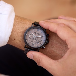 Pu&ograve; includere: Un orologio da polso cronografo nero e marrone con quadrante in legno e cinturino in metallo nero.