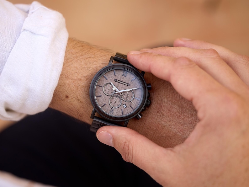 Pu&ograve; includere: Un orologio da polso cronografo nero e marrone con quadrante in legno e cinturino in metallo nero.
