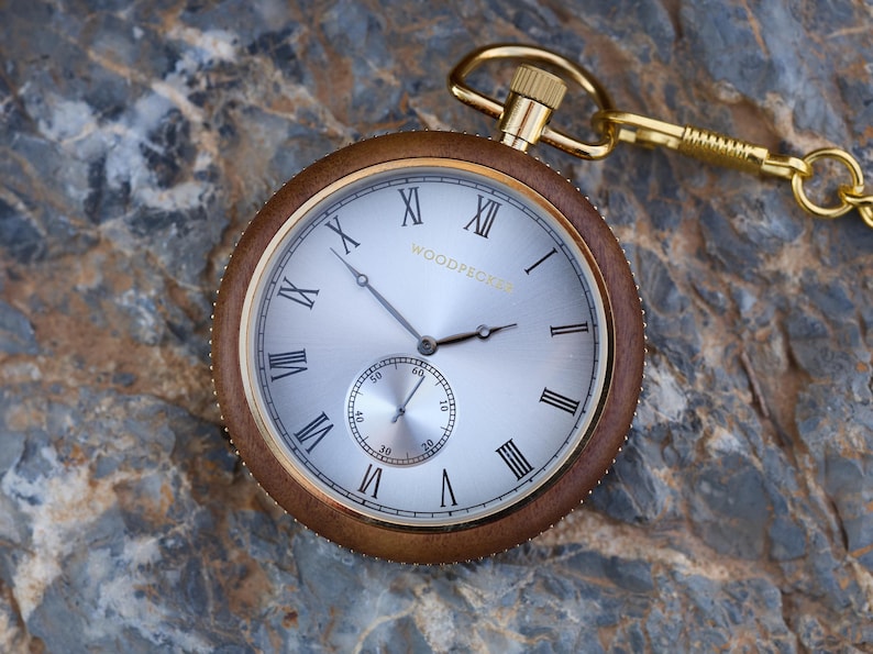 May include: A gold pocket watch with Roman numeral markings on a white face. The watch has a brown wooden case and a gold chain.