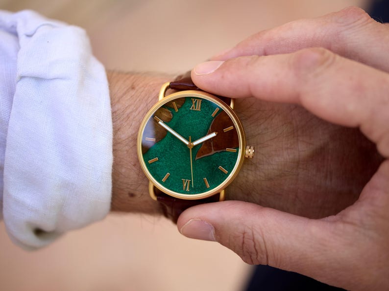 Puede incluir: Un reloj dorado con esfera verde y marr&oacute;n y correa de cuero marr&oacute;n. La esfera del reloj presenta n&uacute;meros romanos y un dise&ntilde;o &uacute;nico. El reloj se lleva en la mu&ntilde;eca.