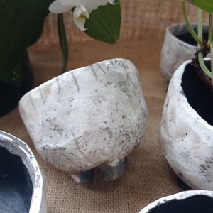 Peut inclure: Un ensemble de quatre pots en céramique blanche avec une finition émaillée craquelée. Les pots ont une forme ronde et une lèvre légèrement évasée. Trois des pots ont un intérieur noir, tandis que le quatrième pot a un intérieur blanc.