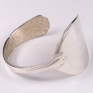 Peut inclure: Un bracelet en argent en forme de cuillère, avec un design incurvé. Le bracelet est fabriqué à partir d'une cuillère, le bol formant la partie principale. Le manche est gravé de motifs floraux et du mot "Chouski".