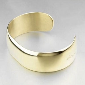 Op de afbeelding: Een gouden armband met een glad, afgerond oppervlak.