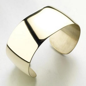 May include: A wide, polished gold cuff bracelet. The bracelet is smooth and has a simple, modern design.