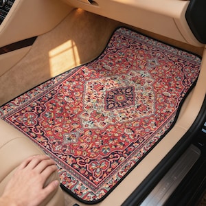 May include: Car floor mat with a traditional Persian rug design. The mat features a red, black, and cream color palette with intricate floral and geometric patterns. The mat is rectangular and fits the car's floor.