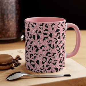 May include: Pink coffee mug with a black leopard print pattern. The mug has a pink rim and handle.
