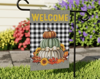 May include: A welcome garden flag with a black and white checkered background. The flag features a stack of three pumpkins with a white bow and sunflowers. The pumpkins are orange, green, and white.