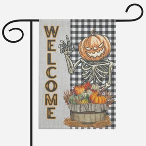 Może przedstawiać: Flaga ogrodowa na Halloween z motywem szkieletu i dyni. Flaga wyświetla słowo "WELCOME" złotymi literami na szarym tle. Kosz z dyniami znajduje się u podstawy, na tle czarno-białego wzoru w kratę.