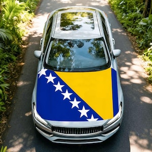 May include: A silver car with a sunroof, viewed from above, driving on a paved road. The hood is decorated with the flag of Bosnia and Herzegovina, featuring a blue triangle, yellow background, and white stars.