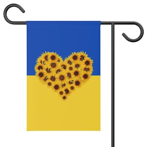 May include: A yellow and blue garden flag with a heart shape made of sunflowers. The flag is attached to a black metal pole.
