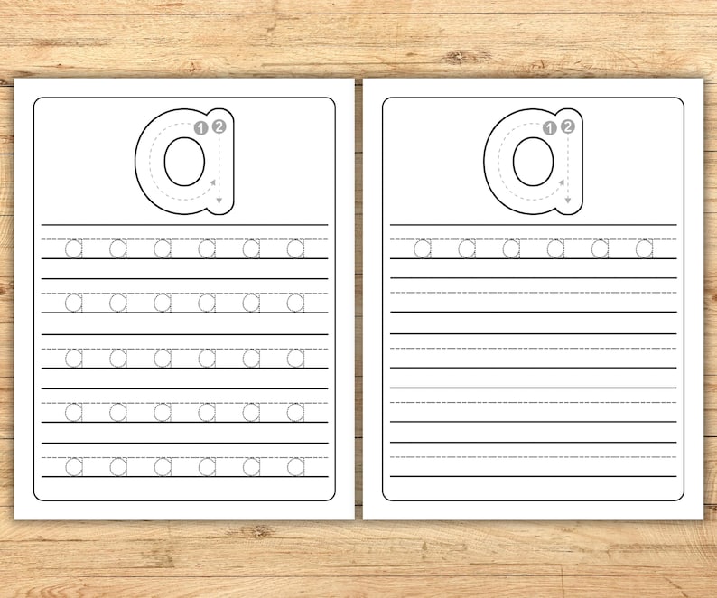 May include: Two white worksheets with the lowercase letter "a" printed on them. The worksheets have a large "a" with numbered arrows for tracing, and lines for practicing writing the letter. The background is a light brown wood.