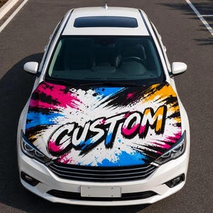May include: White car with a custom hood wrap featuring a colorful splash design in pink, blue, yellow, and black. The word "CUSTOM" is prominently displayed on the hood.