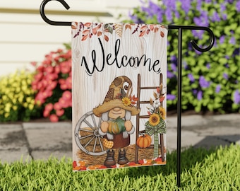 May include: A welcome garden flag with a gnome holding a pumpkin. The gnome is wearing a brown hat with a straw brim and a brown and white dress. The flag has a wooden background with the word "Welcome" written in black.