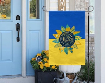May include: A blue and yellow garden flag with a stylized sunflower design. The sunflower is made up of different colored shapes and patterns.